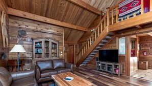 Un interior de madera con un sofá de cuero, una mesa de centro de madera, un televisor y una escalera.