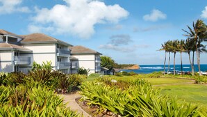 A beachfront hotel with a two-story building, a grassy lawn, and palm trees. - Poipu Sands 411 By Parrish Kauai: Private & end unit (Koloa)