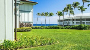 A hotel with a well-maintained lawn, palm trees, and a view of the ocean. - Poipu Sands 411 By Parrish Kauai: Private & end unit (Koloa)