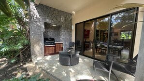 An outdoor kitchen area with a stone wall, a grill, and a dining area with chairs and a table. - 2 BR Condo Centrally Located in Playas del Coco (Playas del Coco)