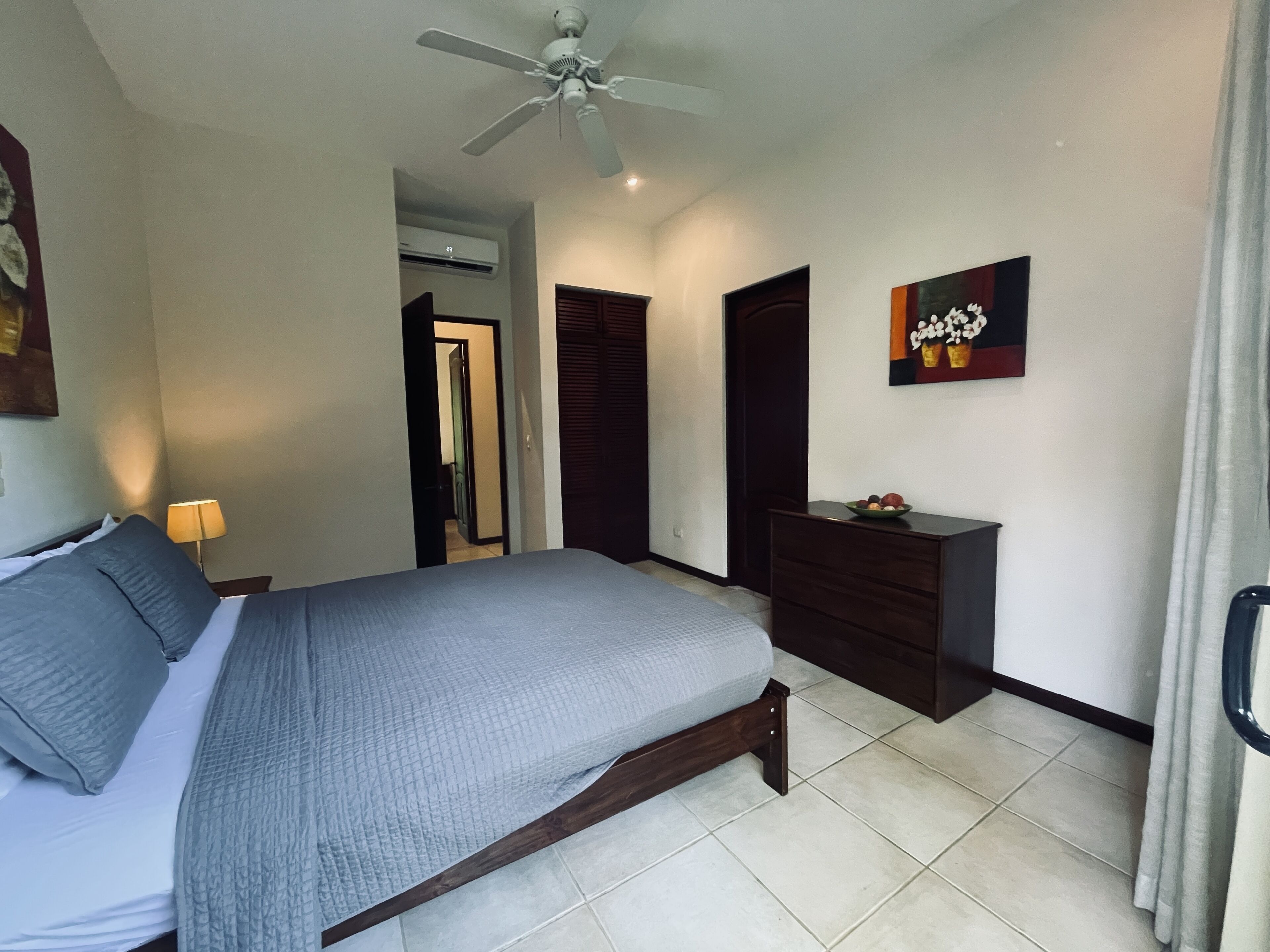 Une chambre à coucher avec un lit, un ventilateur de plafond, une commode et un tableau au mur.