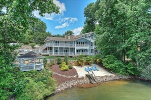 A large house with a covered porch, a small dock, and a pool area with lounge chairs. - Lakefront w/ Beach, Dock, Game Room, Firepit, Kayaks, views (Mooresville)