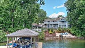 Une propriété au bord du lac, dotée d’un quai, d’un abri à bateaux et d’une grande maison avec un balcon offrant une vue sur l’eau.