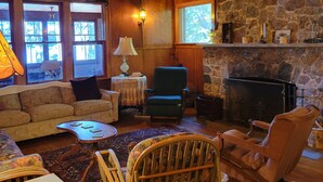 A cozy living room with a stone fireplace, wooden ceiling, and a bookshelf. - Classic Northwoods Cabin Experience Awaits You (Lac du Flambeau)