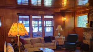 A cozy living room with wooden walls, a sofa, a coffee table, a bookshelf, and a fireplace. - Classic Northwoods Cabin Experience Awaits You (Lac du Flambeau)
