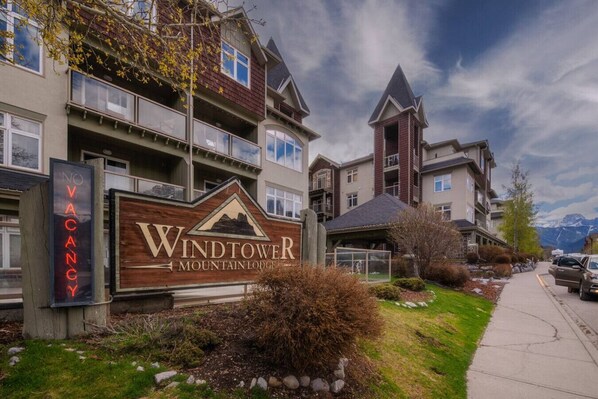 A mountain lodge with a 'NO VACANCY' sign, a prominent mountain logo, and a view of the mountains in the background.