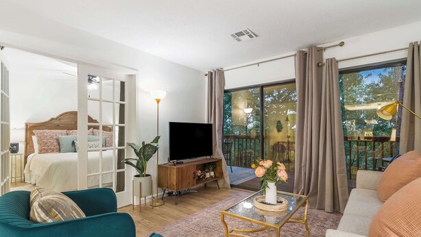 Ein modernes Wohnzimmer mit einer Couch, einem Couchtisch, einem Fernseher und einem Balkon mit Vorhängen.