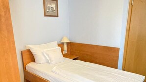 A single bed with a wooden headboard, white bedding, and a bedside table with a lamp. - Single room (Pulheim)