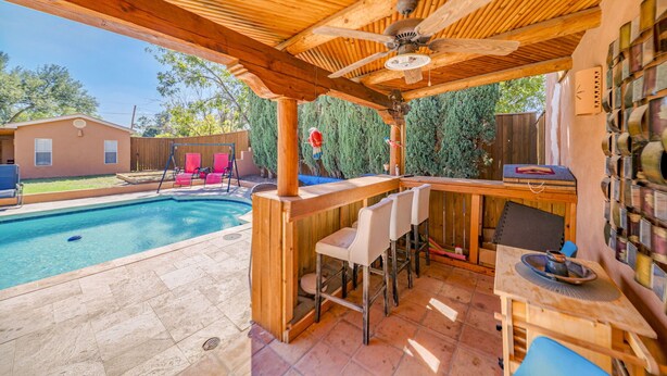 A wooden outdoor bar area with a pool, bar stools, and a ceiling fan. - Right At Home-Midland Adobe Compound with Pool and Fire Pits and Billiards (Midland)