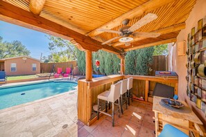 Un espace bar extérieur en bois, doté d’une piscine, de tabourets de bar et d’un ventilateur de plafond.