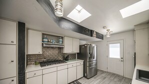 A modern kitchen with white cabinets, a stainless steel refrigerator, and a skylight. - Right At Home-Midland Adobe Compound with Pool and Fire Pits and Billiards (Midland)