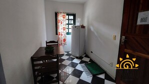 Et lille køkken med et køleskab, et bord med stole og et vindue med blomstret gardin.