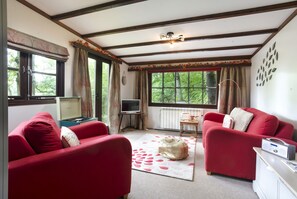 A cozy living room with red sofas, a TV, and a fireplace. - Low Tarn Lodge - One Bedroom Apartment, Sleeps 2 (Skelwith)