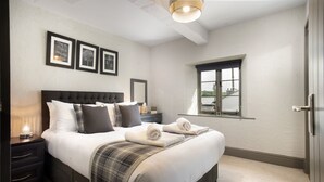 Una cama bien tendida con una manta de cuadros, una lámpara de noche y cuadros en la pared.