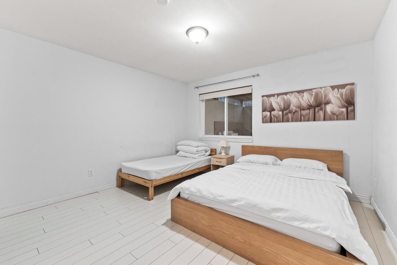Un dormitorio con una cama grande, una cama más pequeña, una mesita de noche, una ventana con persianas y una obra de arte colgada en la pared.