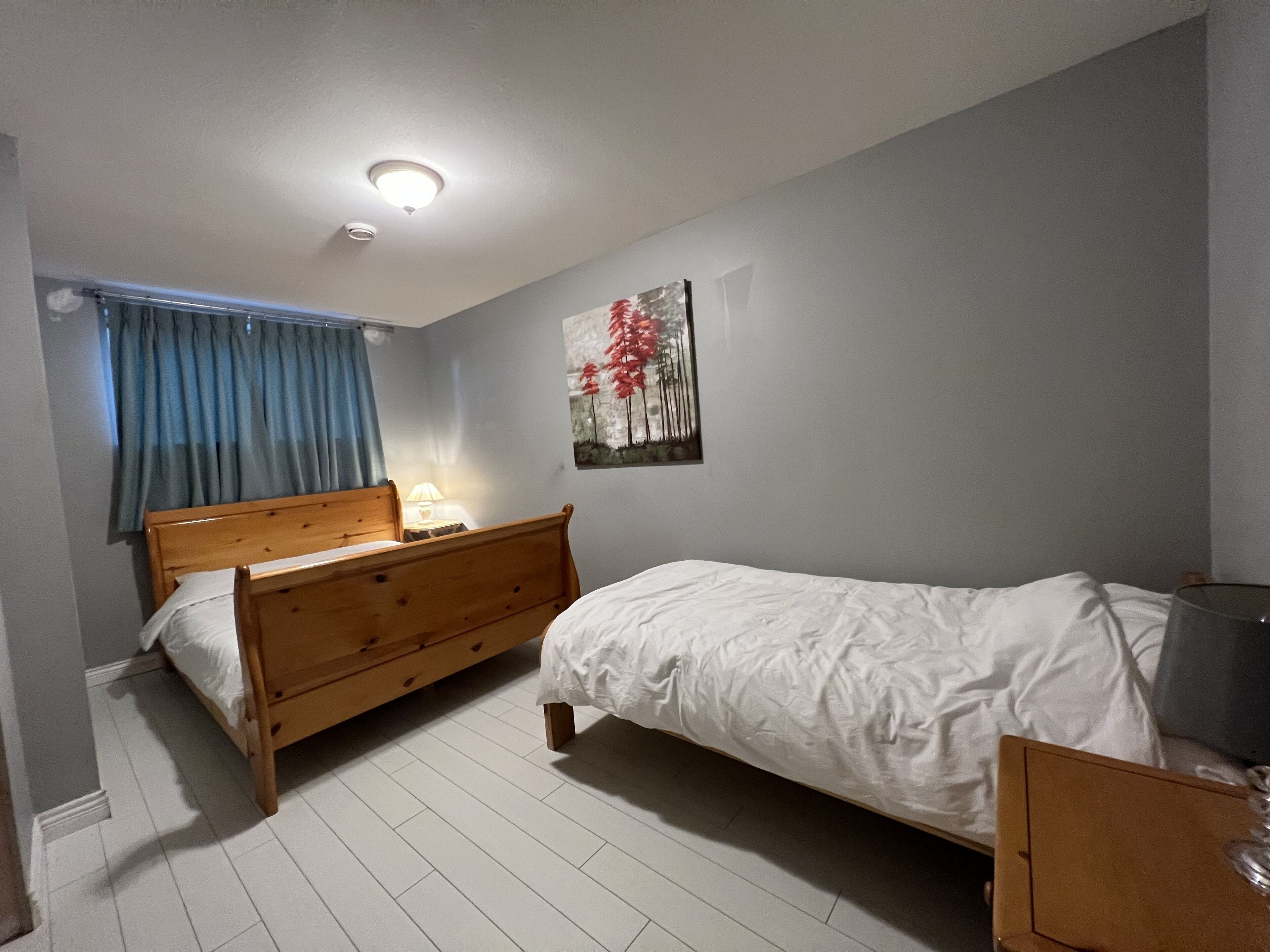 A bedroom with a wooden bed, a smaller bed, a nightstand, a lamp, and a painting on the wall.