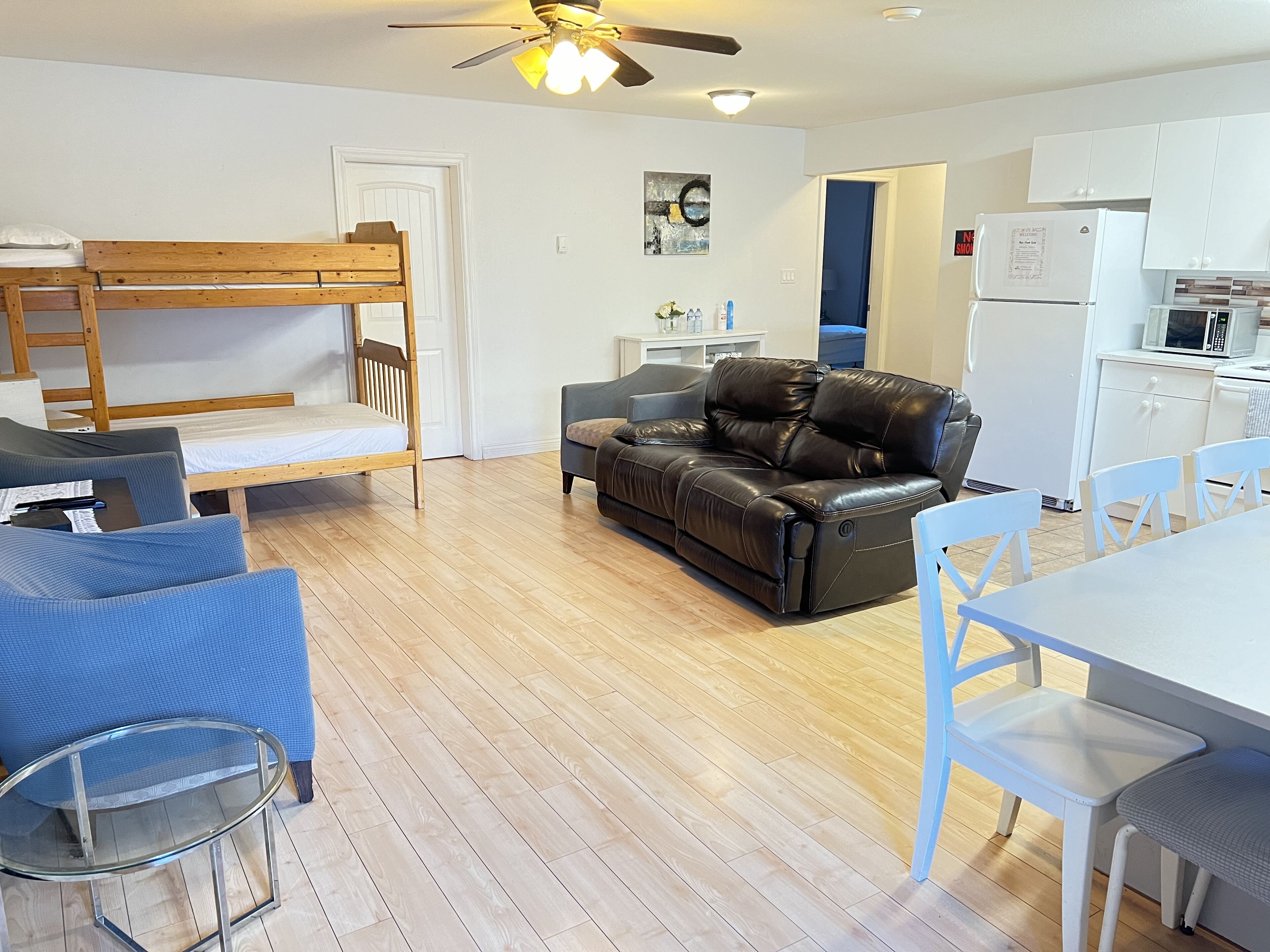 A compact living space with a bunk bed, a leather sofa, a dining table with chairs, and a kitchenette.