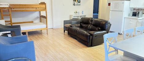 A compact living space with a bunk bed, a leather sofa, a dining table with chairs, and a kitchenette.