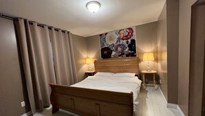 A hotel room with a wooden bed, two bedside lamps, a floral artwork above the bed, and beige curtains.