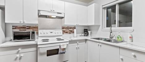 Una cocina moderna con armarios blancos, microondas, estufa y un lavaplatos.