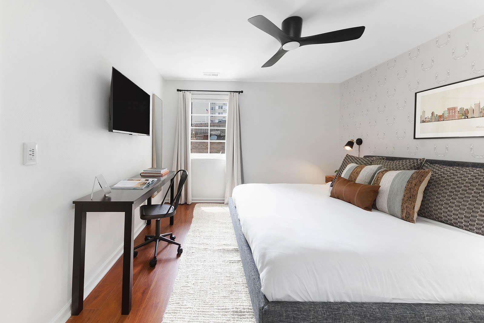 Habitación de hotel moderna con cama, escritorio, silla y ventilador de techo.