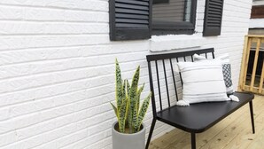 A black metal bench with white cushions against a white brick wall, next to a potted plant with variegated leaves.
