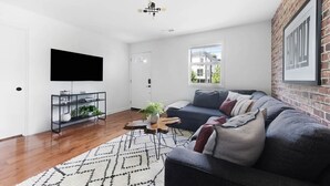 A modern living room with a dark grey sofa, a mounted TV, a glass coffee table, and a patterned rug.