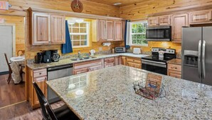 A kitchen with wooden cabinets, granite countertops, a stainless steel refrigerator, and a microwave. - HUGE 7BD Lodge IN TOWN +Pool Table + Views (Gatlinburg)