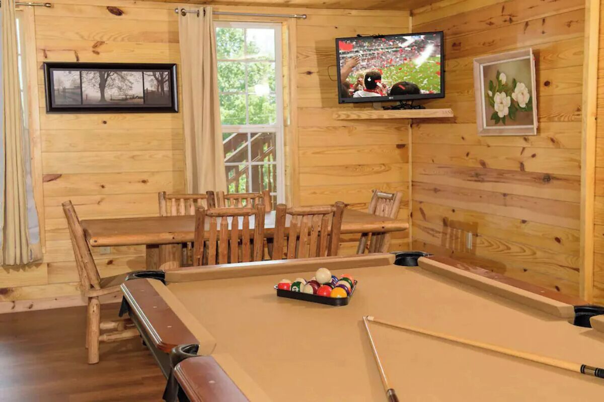 Une pièce en bois comprenant une table de billard, un téléviseur fixé au mur et un coin repas avec des meubles en bois.