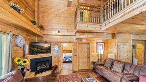 A spacious log cabin interior with a living room, a fireplace, a balcony, and a second-floor bedroom. - HUGE 7BD Lodge IN TOWN +Pool Table + Views (Gatlinburg)
