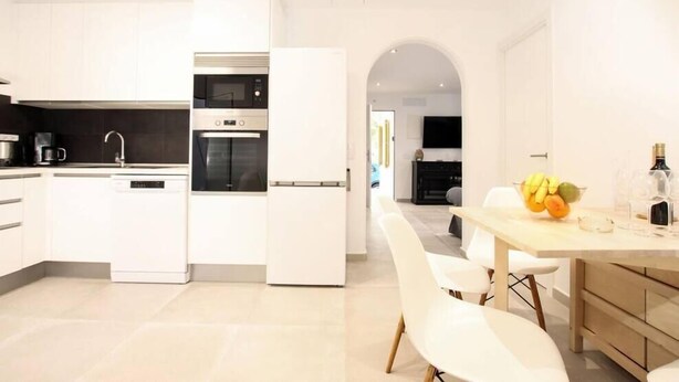 Une cuisine moderne avec des meubles blancs, un four encastré et un coin repas comprenant une table et des chaises.