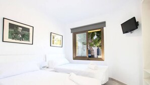 Une chambre d’hôtel avec deux lits, un téléviseur fixé au mur et une fenêtre donnant sur un arbre et un immeuble.