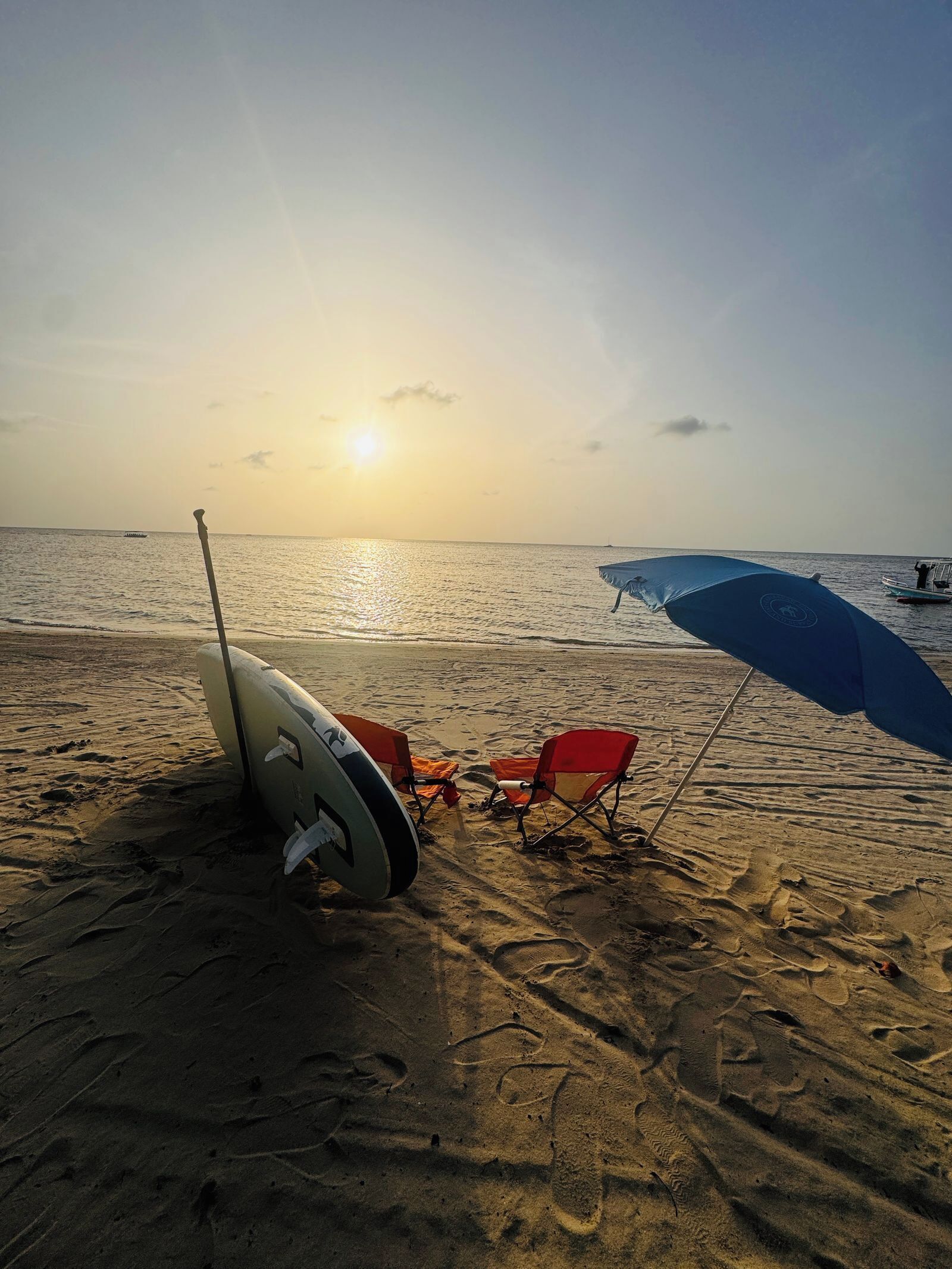 Eine Strandansicht mit einem Surfbrett, einem roten Liegestuhl und einem blauen Sonnenschirm.