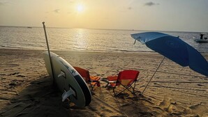 Escena de playa con una tabla de surf, una silla de playa roja y una sombrilla azul.