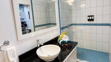 Une salle de bain avec un lavabo blanc, un plan de toilette noir et une douche fermée par des parois en verre.