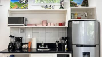 Una cocina moderna con un refrigerador de acero inoxidable, un microondas y una cafetera. Hay armarios, un lavamanos y una ventana con vista a zonas verdes.