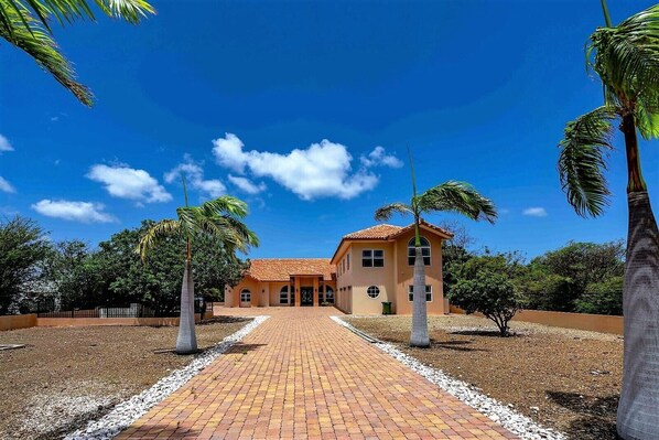 A two-story building with a tiled roof, surrounded by palm trees and a paved walkway. - Villa Magic Time - Oceanfront (Willibrordus)