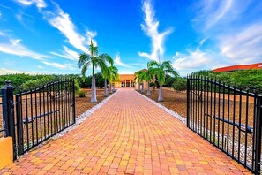 A paved pathway leading to a building with a red roof, flanked by palm trees and black metal gates. - Villa Magic Time - Oceanfront (Willibrordus)