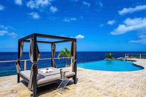 A beachside infinity pool with a canopy bed and palm trees. - Villa Magic Time - Oceanfront (Willibrordus)