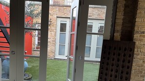 A room with a large sliding glass door leading to a backyard with a brick wall, a red fence, and a small garden. - Exclusive Apartment with terrace, garage, gym in Georgian Residence well located (London)
