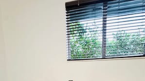 A room with a round table and two chairs with woven backs, a window with blinds, and a view of greenery outside.
