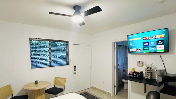 A hotel room with a bed, a desk, a chair, a television, and a ceiling fan.