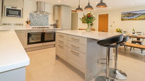 A modern kitchen with a central island, stainless steel appliances, and pendant lighting. - Ladstock Cottage (Keswick)