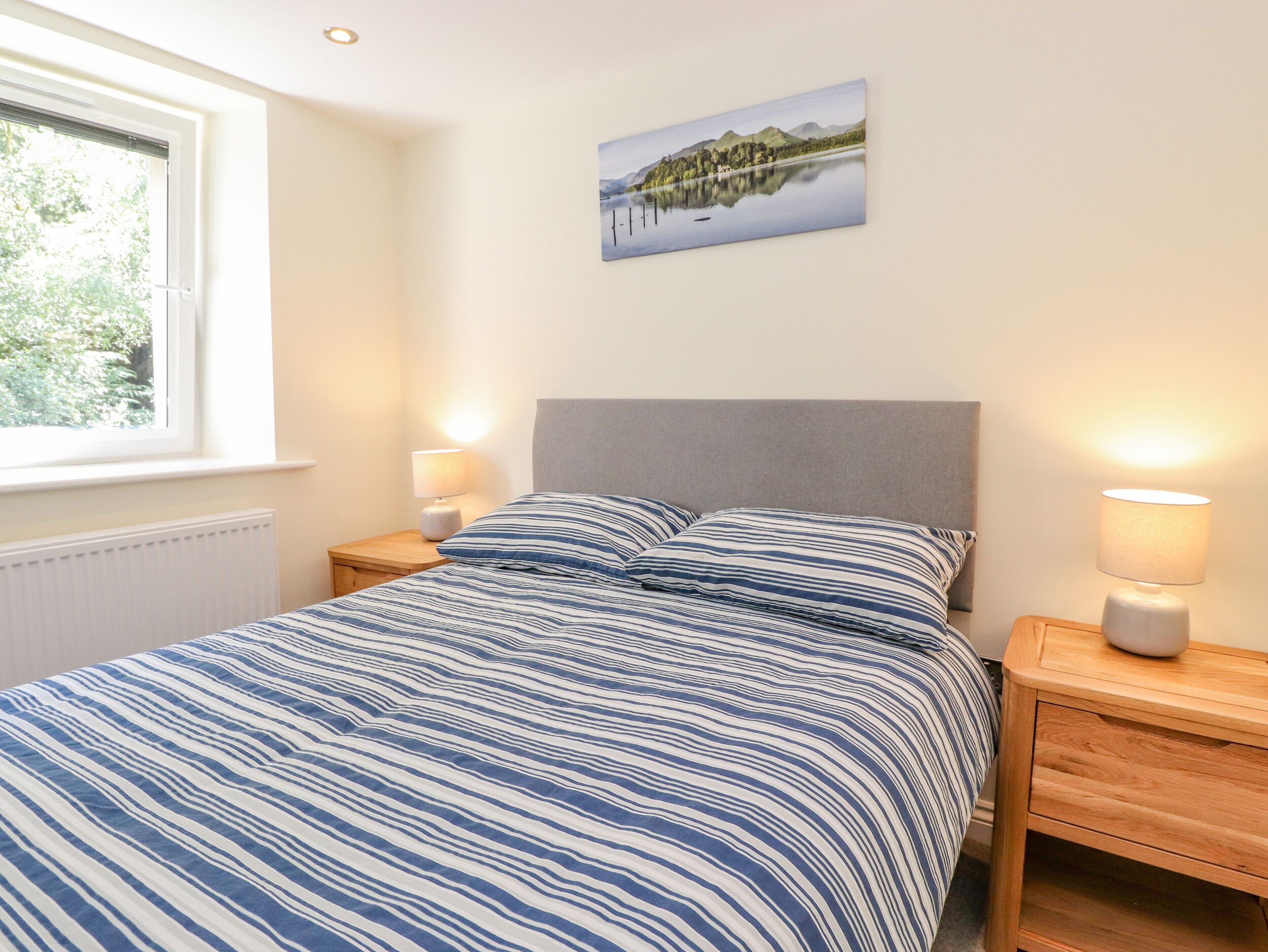 Une chambre à coucher avec un lit, deux tables de chevet avec des lampes, une fenêtre et un tableau au mur.