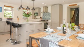 A modern kitchen with a central island, bar stools, and a dining table set for six. - Ladstock Cottage (Keswick)