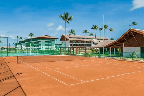 A tennis court with a net, surrounded by a fence and palm trees. - Carpediem - Moderno apartamento no Cupe (Ipojuca)