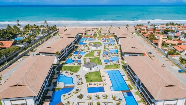 Um resort com várias piscinas, um pátio central e vista para a praia.