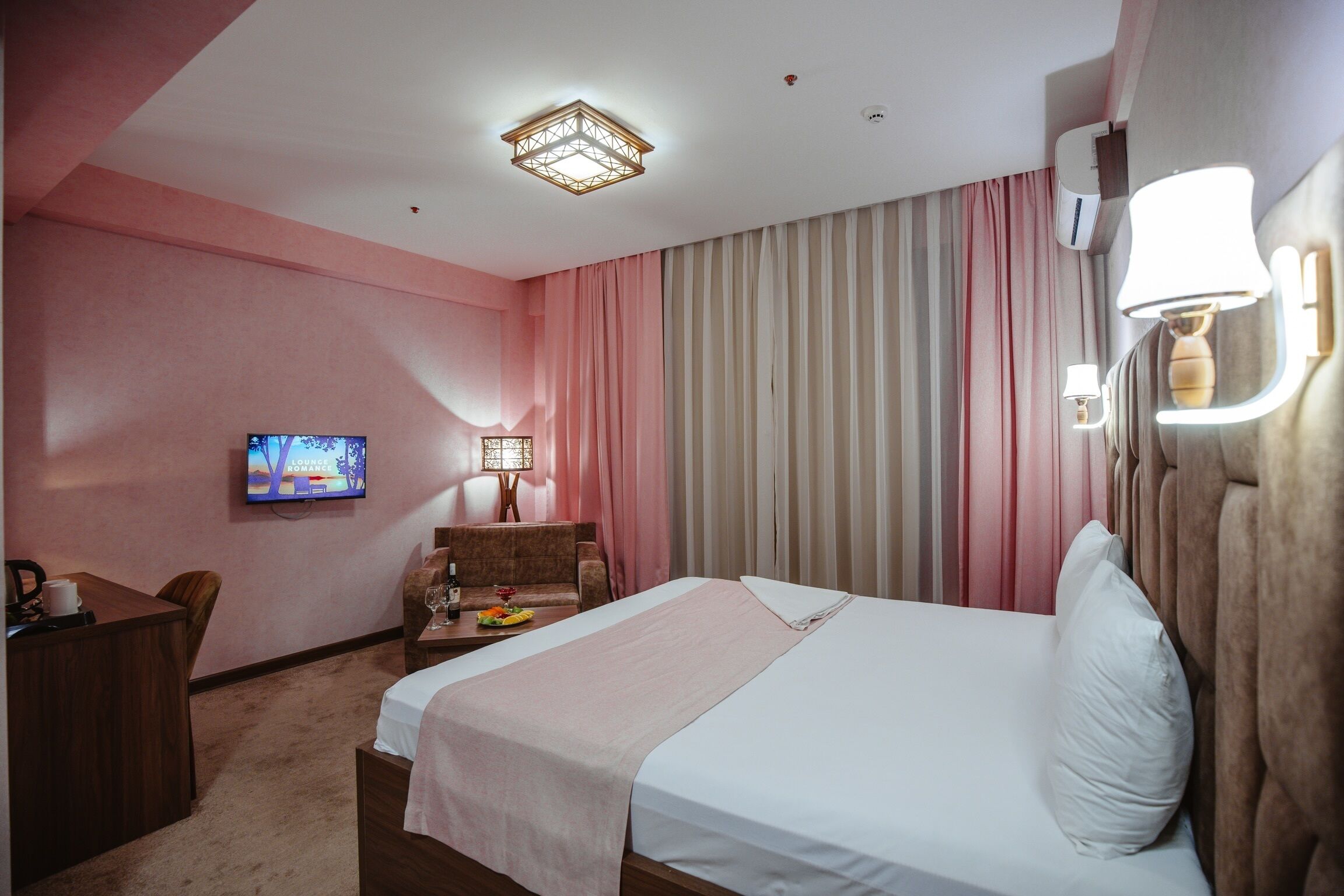 A hotel room with a bed, a desk, a chair, a TV, and a lamp.