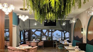 A restaurant with hanging plants, round tables, and chairs. - Alison Hotel Baku (Baku)