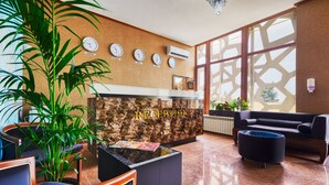 A reception area with a marble reception desk, clocks indicating different time zones, a large window with geometric patterns, and a modern seating arrangement. - Alison Hotel Baku (Baku)